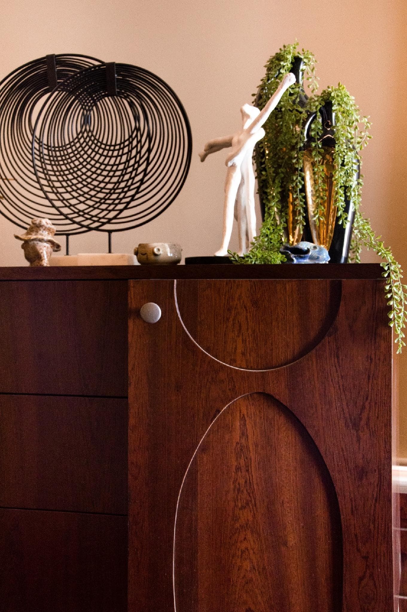 A wood cabinet styled with ceramic vessels and a wire sculpture.