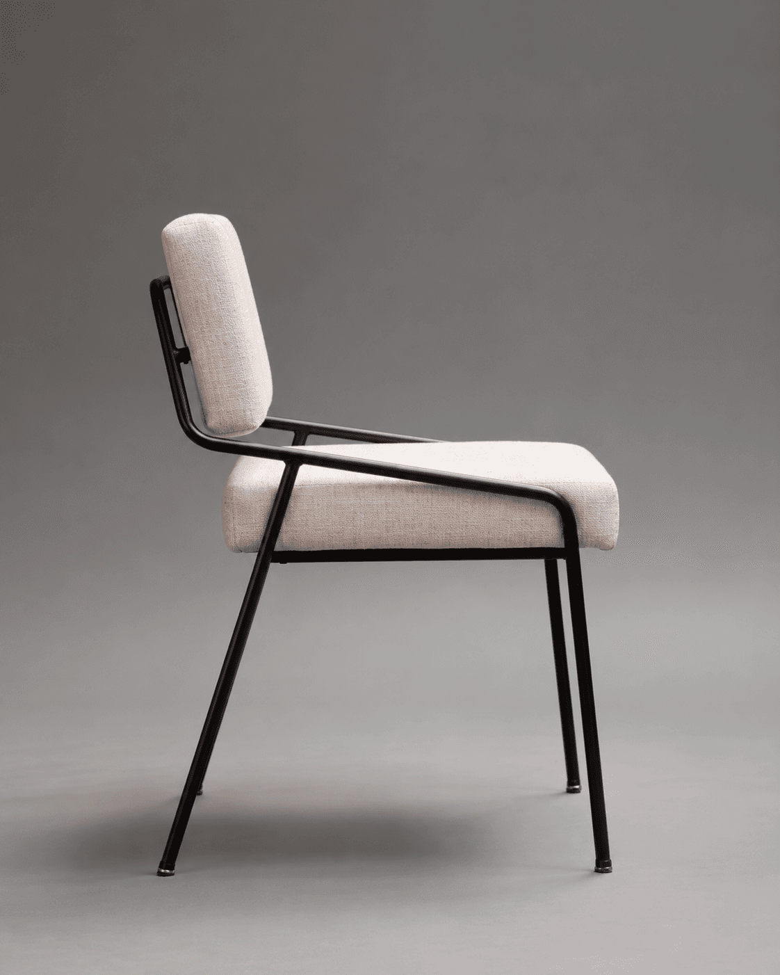 KAIRO modern dining chair shown in side profile with a slim black metal frame and neutral upholstered seat and back.